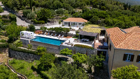 Daytime aerial view of the stone estate, infinity pool, and coastline.