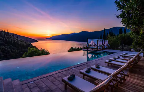 Infinity pool and loungers silhouetted against an Adriatic sunset.