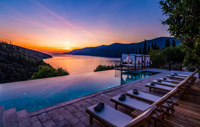 Infinity pool and loungers silhouetted against an Adriatic sunset.