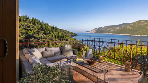 Shaded garden terrace with seating beneath Mediterranean trees.